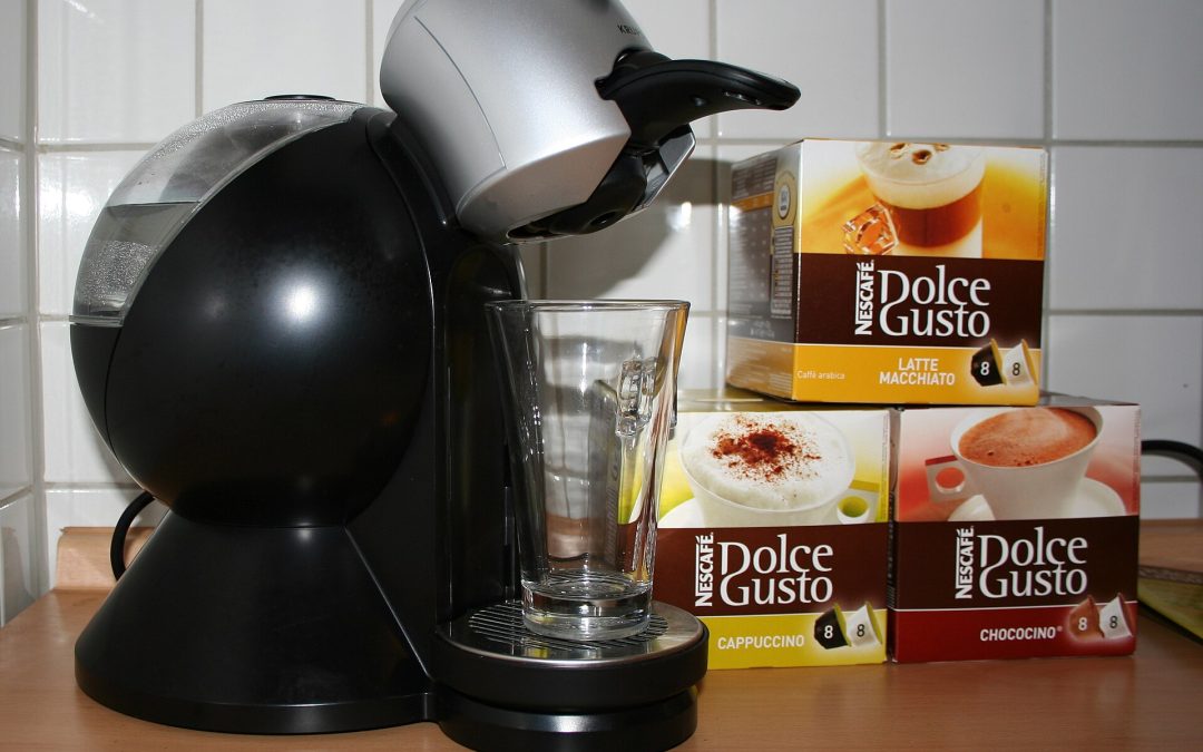 Cafetera Nescafé Dolce Gusto negra junto a cajas de cápsulas de latte macchiato, capuchino y chococino